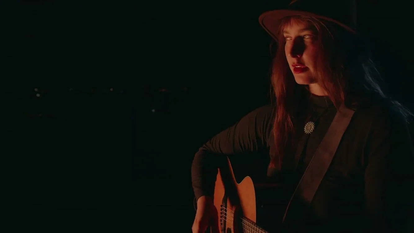 Sarah Osborne plays guitar in warm light against a dark night background in Autumn Sun.