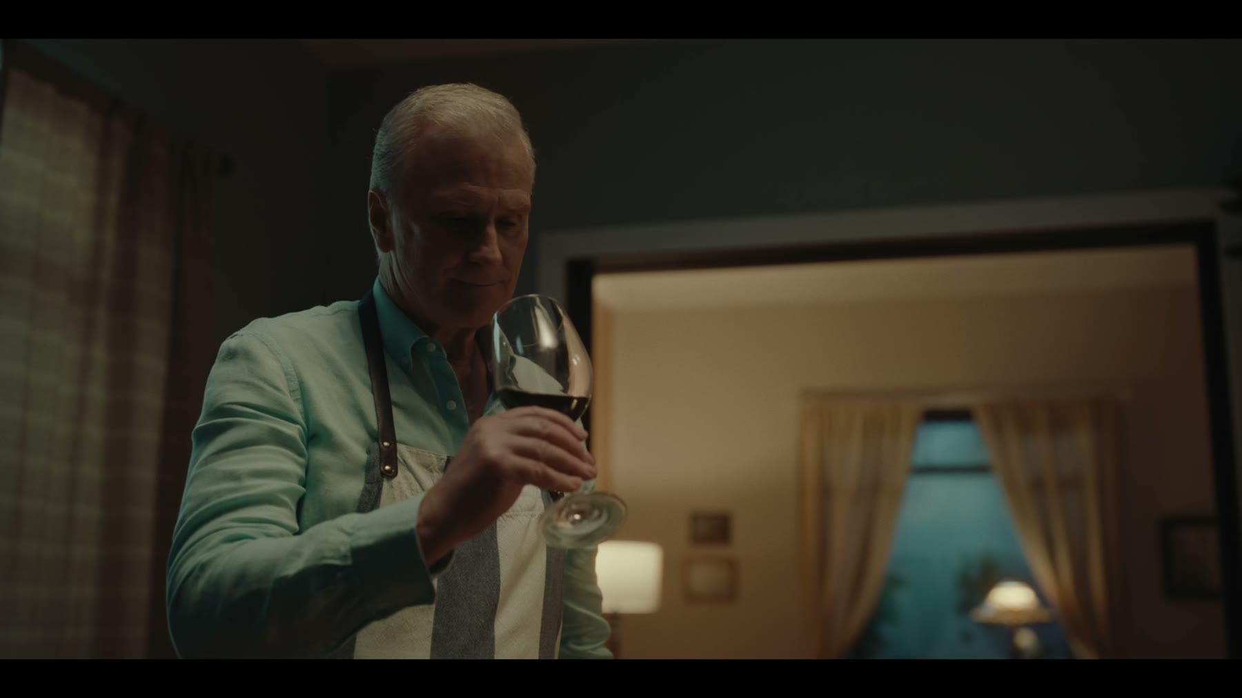 Two men confront one another in a carefully lit apartment interior.