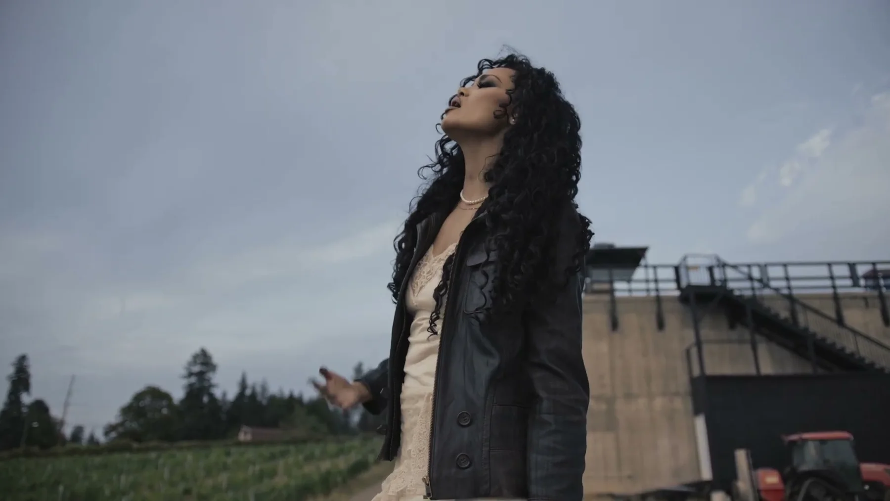 A woman sings outside near a weathered rural building.