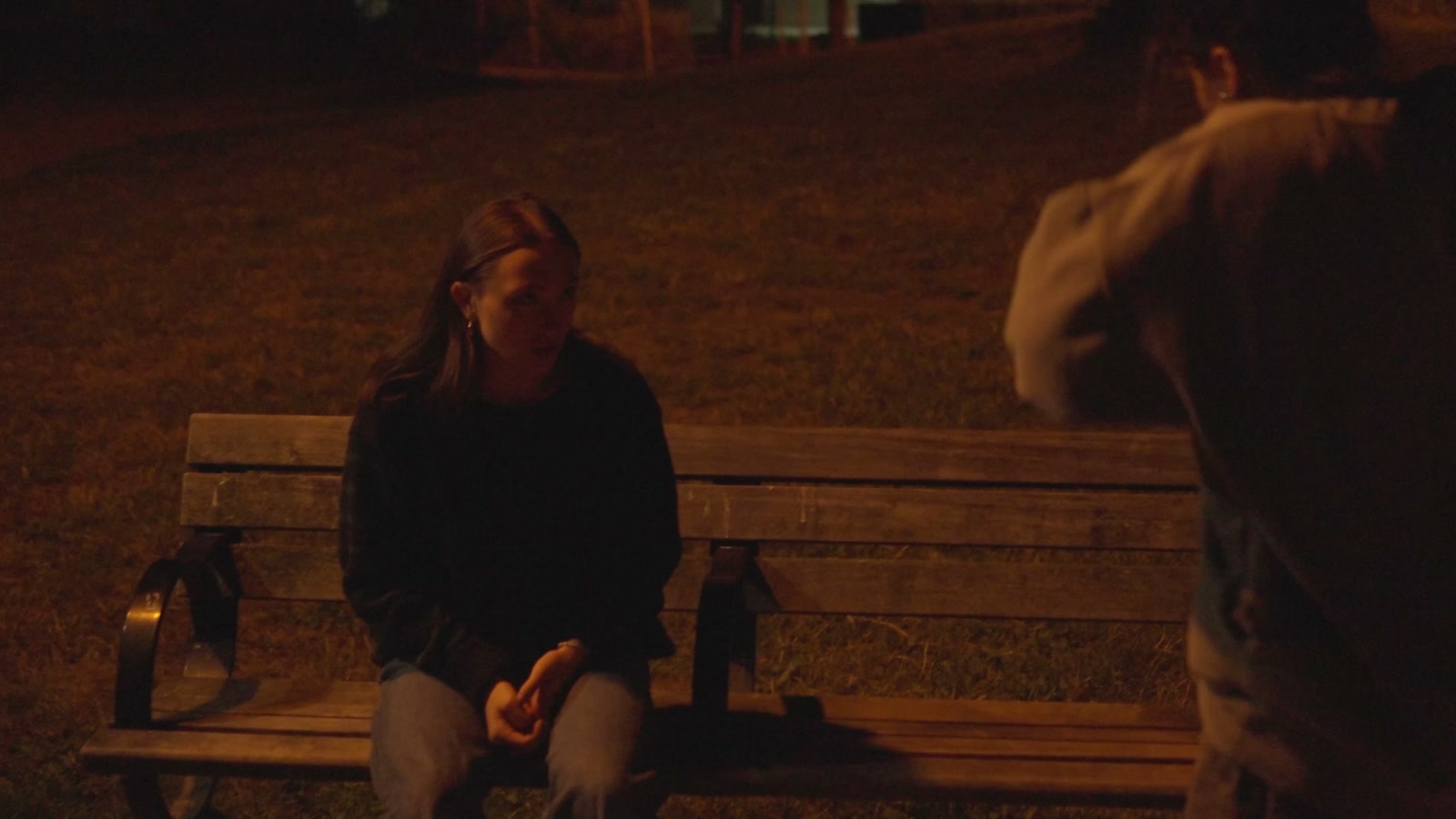 A quiet exchange beside a park bench at night.