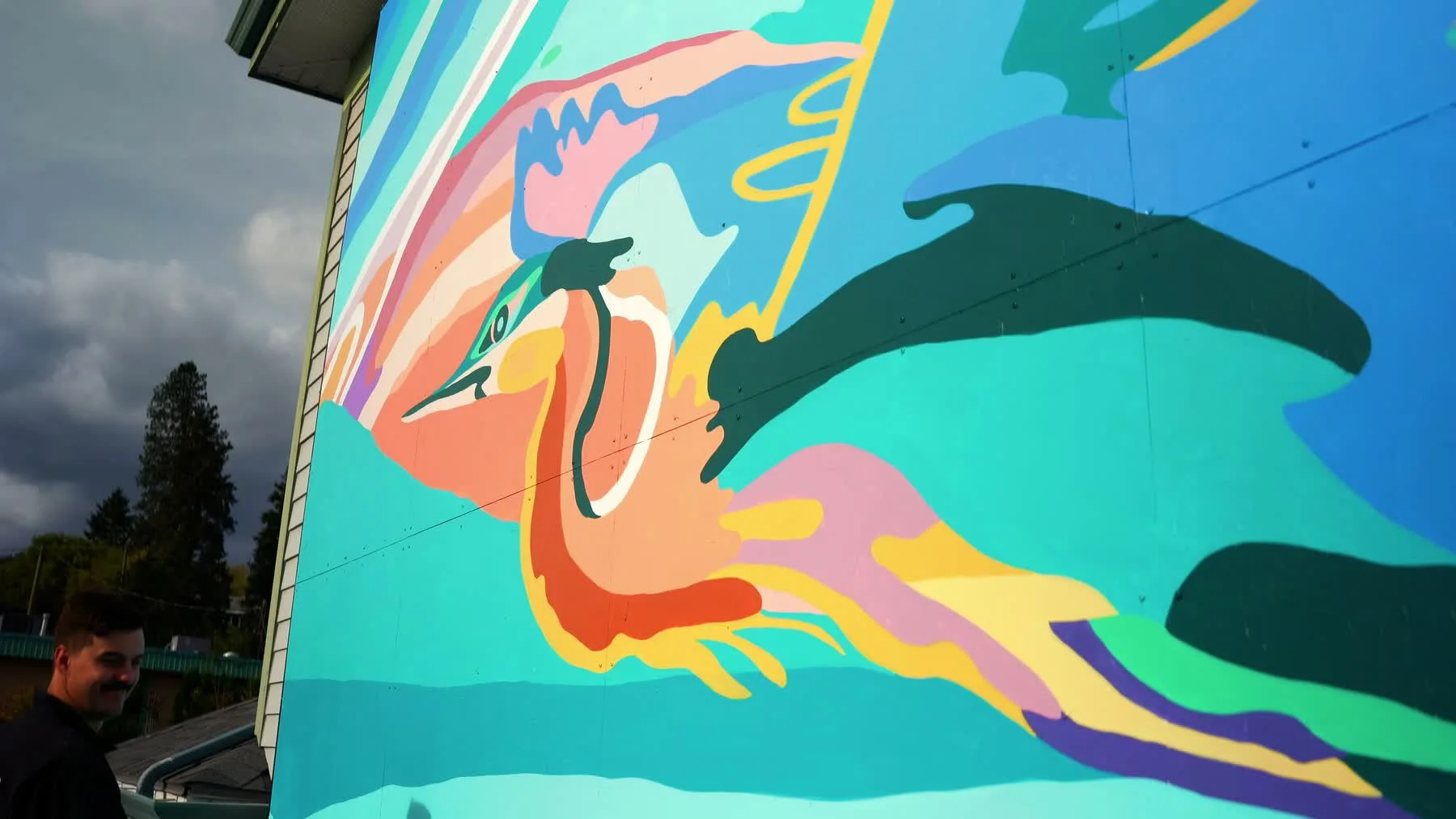 A colourful bird mural rises above one of the Jomae artists at the base of the wall.