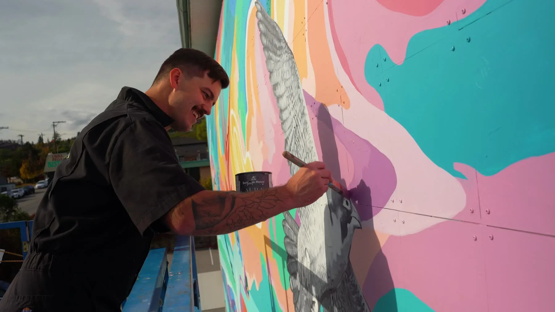 Dylan Ranney paints a bird detail while working from a lift beside the mural.