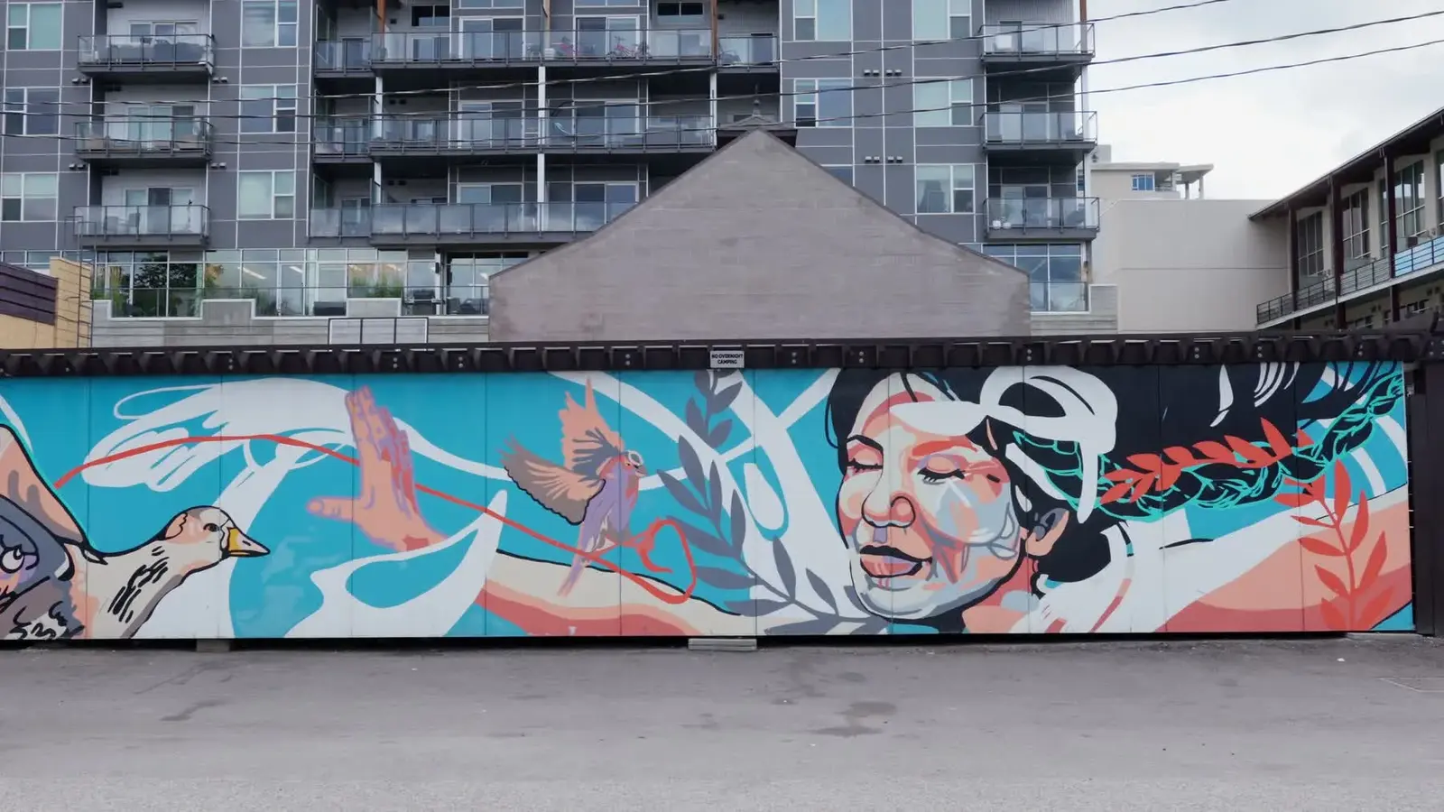 A long public mural shows birds, a portrait and flowing coloured lines across an urban wall.