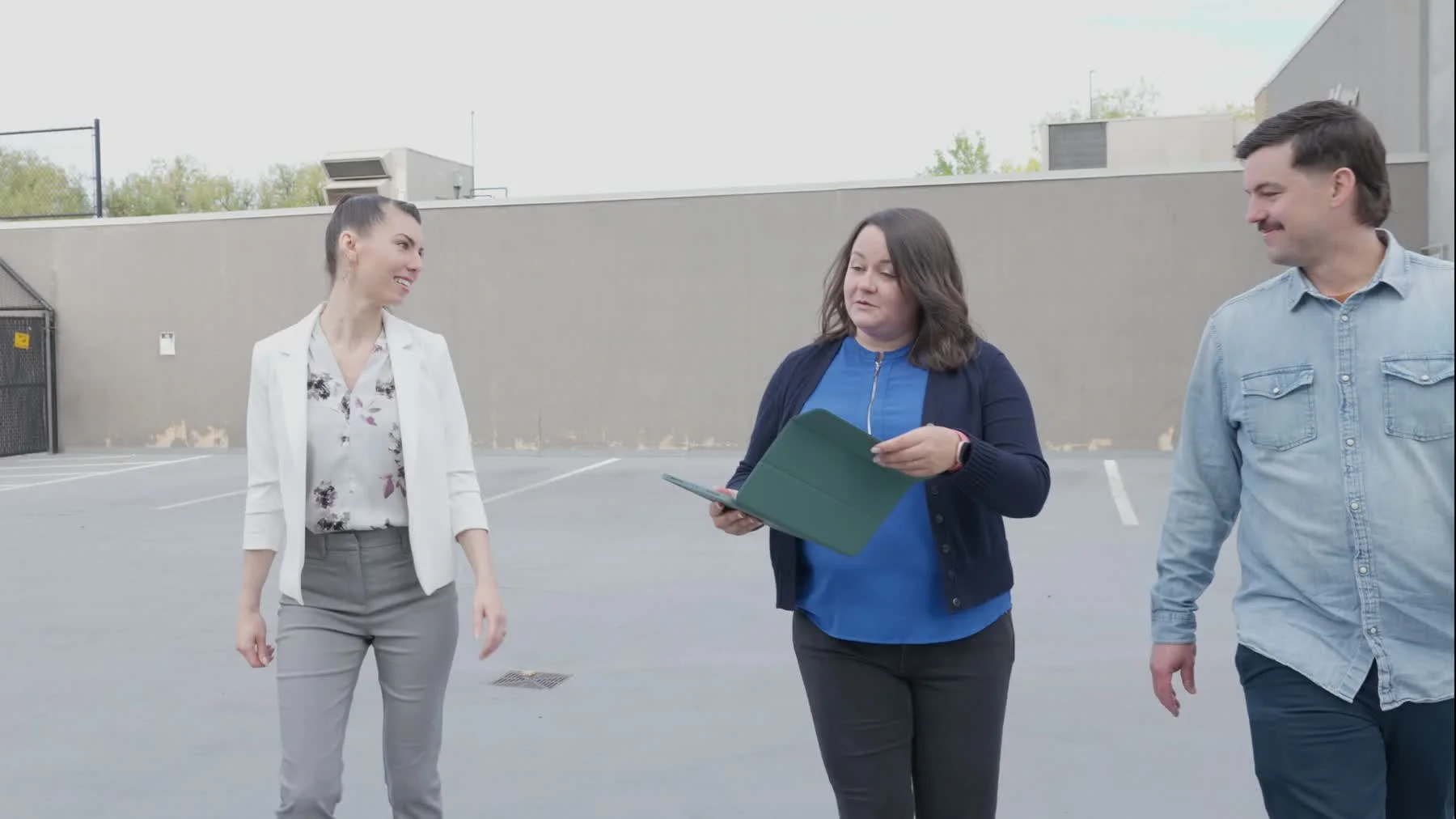 Liz and Dylan Ranney walk a blank exterior wall with a client during a mural consultation.