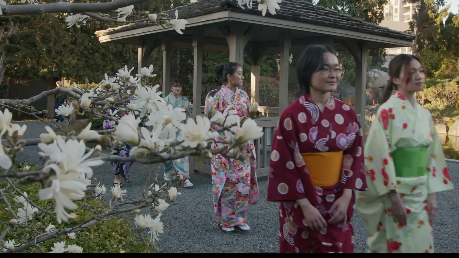 Three women in colourful kimono stand beside white blossoms in Kasugai Gardens.
