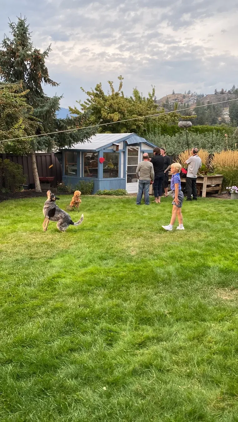 Three Hearts yard scene with young actors, family members and dogs gathered near the garden.